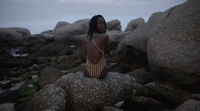 a woman sitting on top of a rock next to a body of water