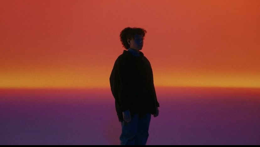 a man standing in front of an orange and purple sky