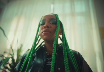 a woman with green dreadlocks standing in front of a window