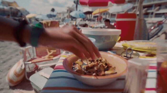 a person reaching for a bowl of food on a beach