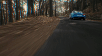 a blue car driving down a road next to a forest