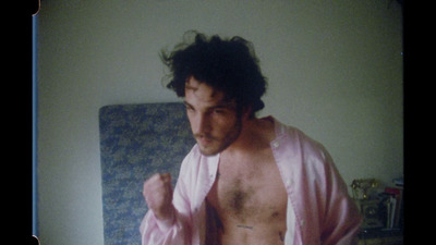 a man in a pink robe standing in front of a bed