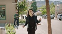 a woman walking down a sidewalk next to a tree