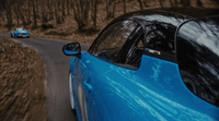 a blue car driving down a road next to a forest