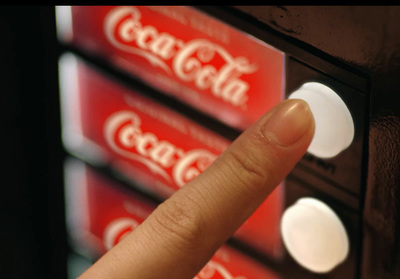 a person is pointing at a coca cola vending machine