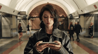 a woman standing in a subway looking at her cell phone