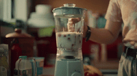 a person pouring something into a blender in a kitchen