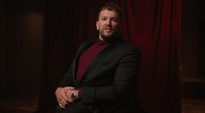 a man sitting in a chair in front of a red curtain