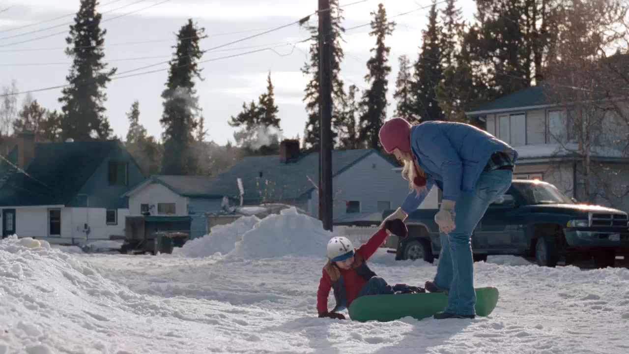 a woman helping a child on a snowboard in the snow