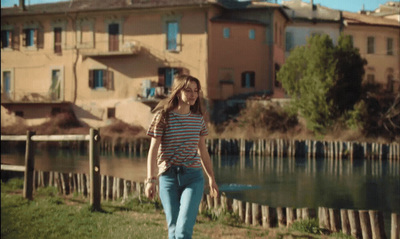 a girl in a striped t-shirt walking by a river