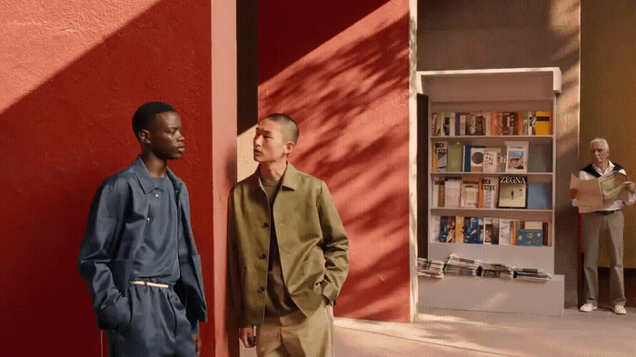 two men standing next to each other in front of a red wall