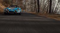 a blue car driving down a road next to a forest