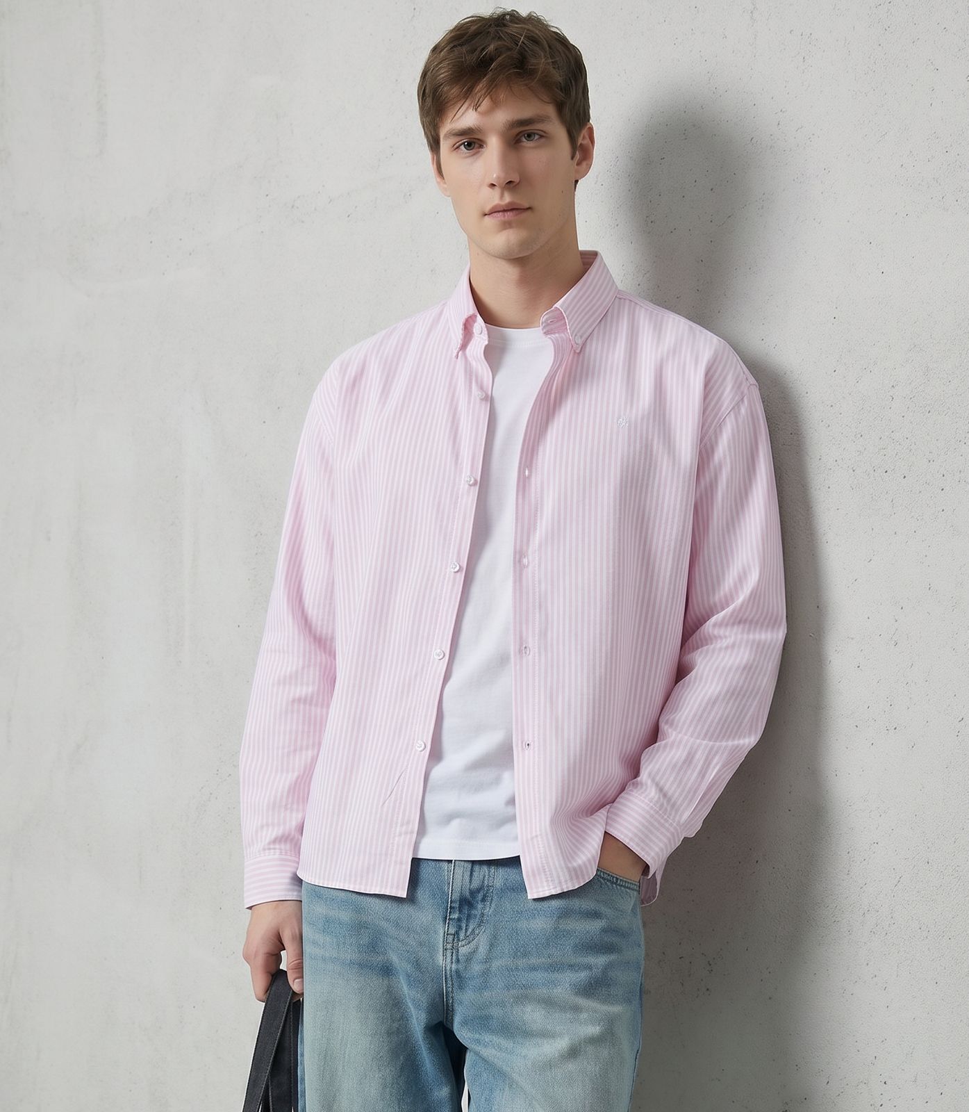 a man in a pink shirt and jeans leaning against a wall