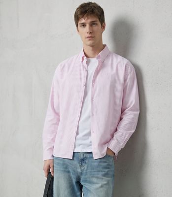 a man in a pink shirt and jeans leaning against a wall