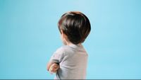 a little boy standing in front of a blue background