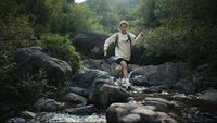 a man walking across a river surrounded by rocks