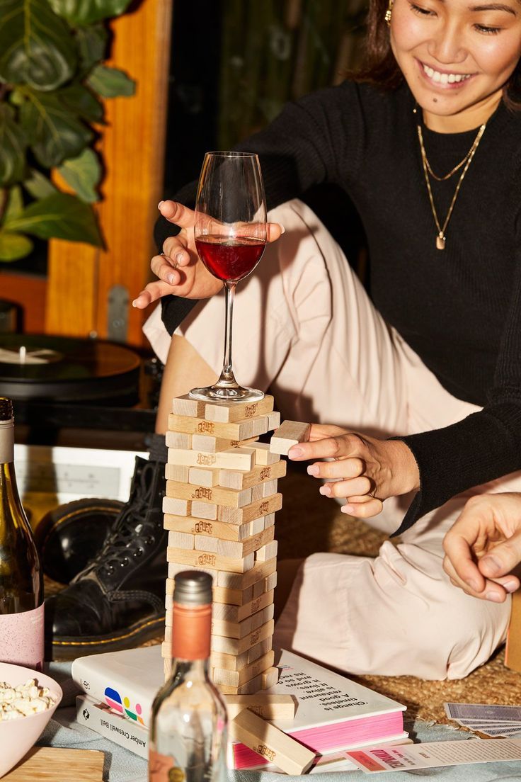 a woman holding a glass of wine next to a tower of blocks