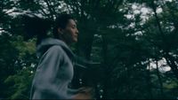 a woman running through a forest with trees in the background