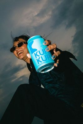 a woman is holding a can of klu kluk on a cloudy day