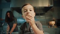 a young boy eating something while standing in a kitchen