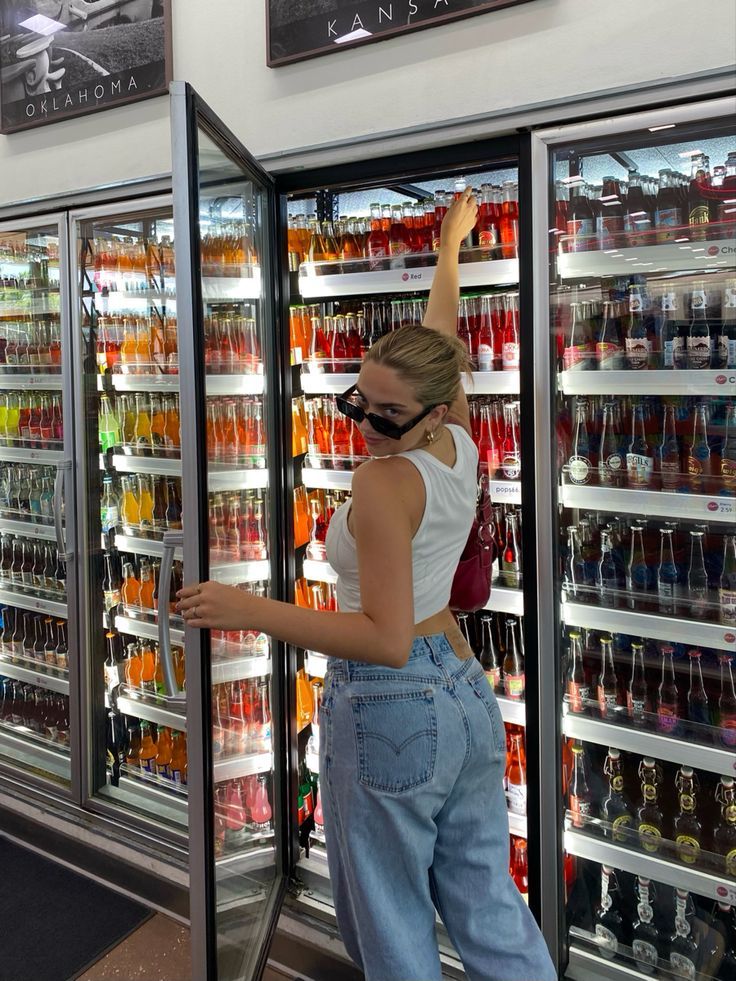 a woman standing in front of a refrigerator filled with drinks