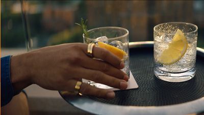 a person holding a slice of lemon next to a glass of water