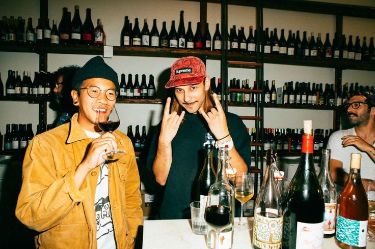 a couple of men standing next to each other in front of bottles of wine