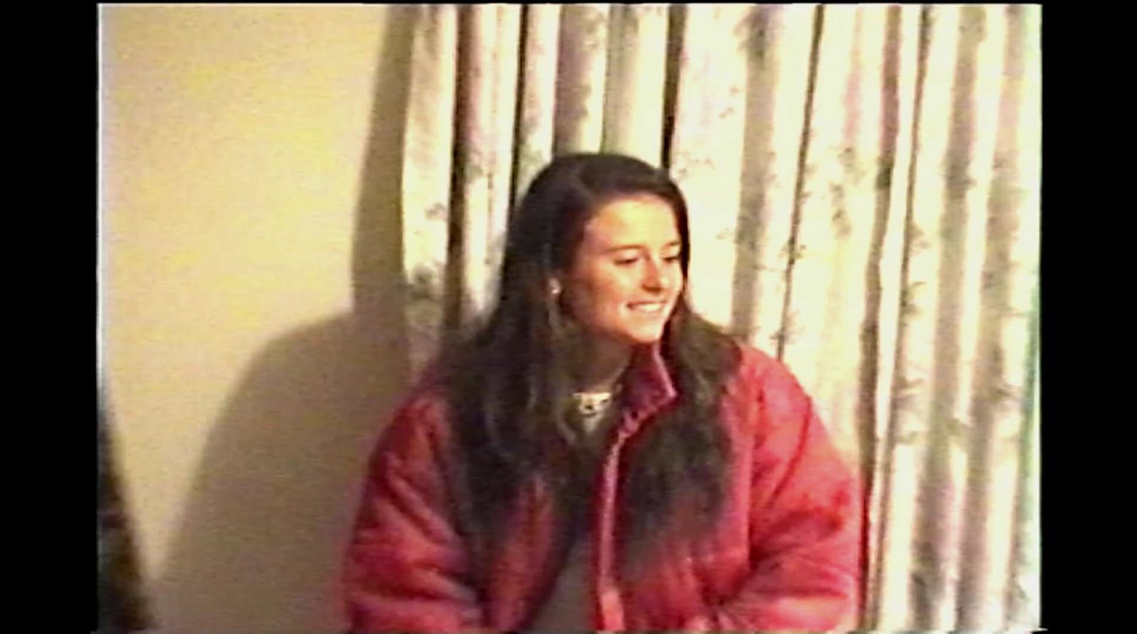 a woman in a red jacket standing in front of a window