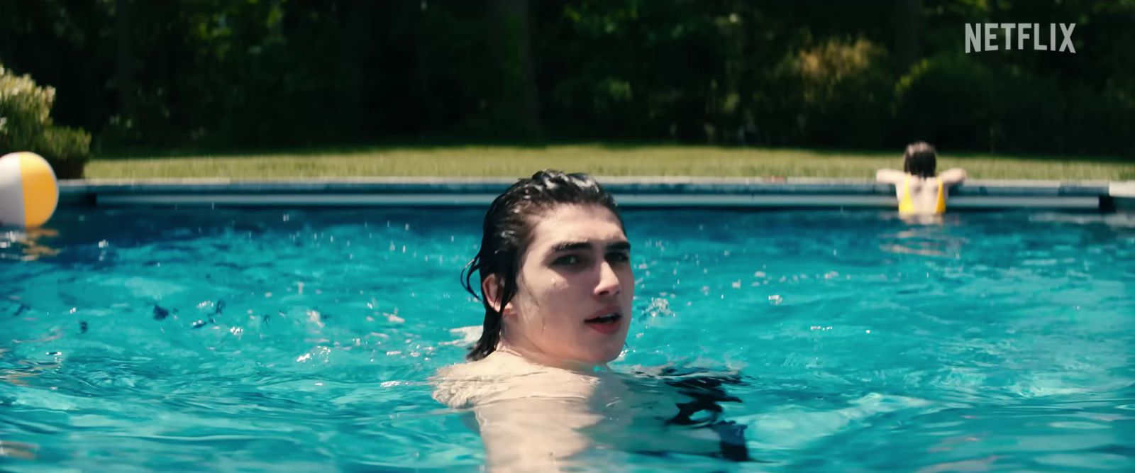 a woman swimming in a pool with a ball in the background