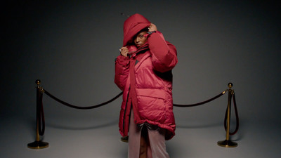 a woman in a pink coat is standing in front of a barrier