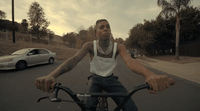 a man riding a bike down a street next to a white car