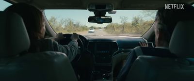 a man driving a car down a road next to a forest