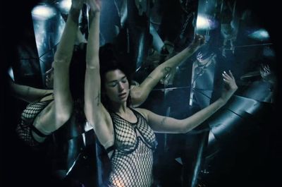 a woman in a fishnet bodysuit dancing in front of a mirror