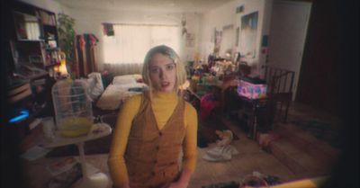 a woman standing in a messy room with a birdcage