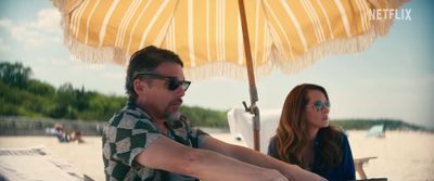 a man and a woman sitting on a beach under an umbrella