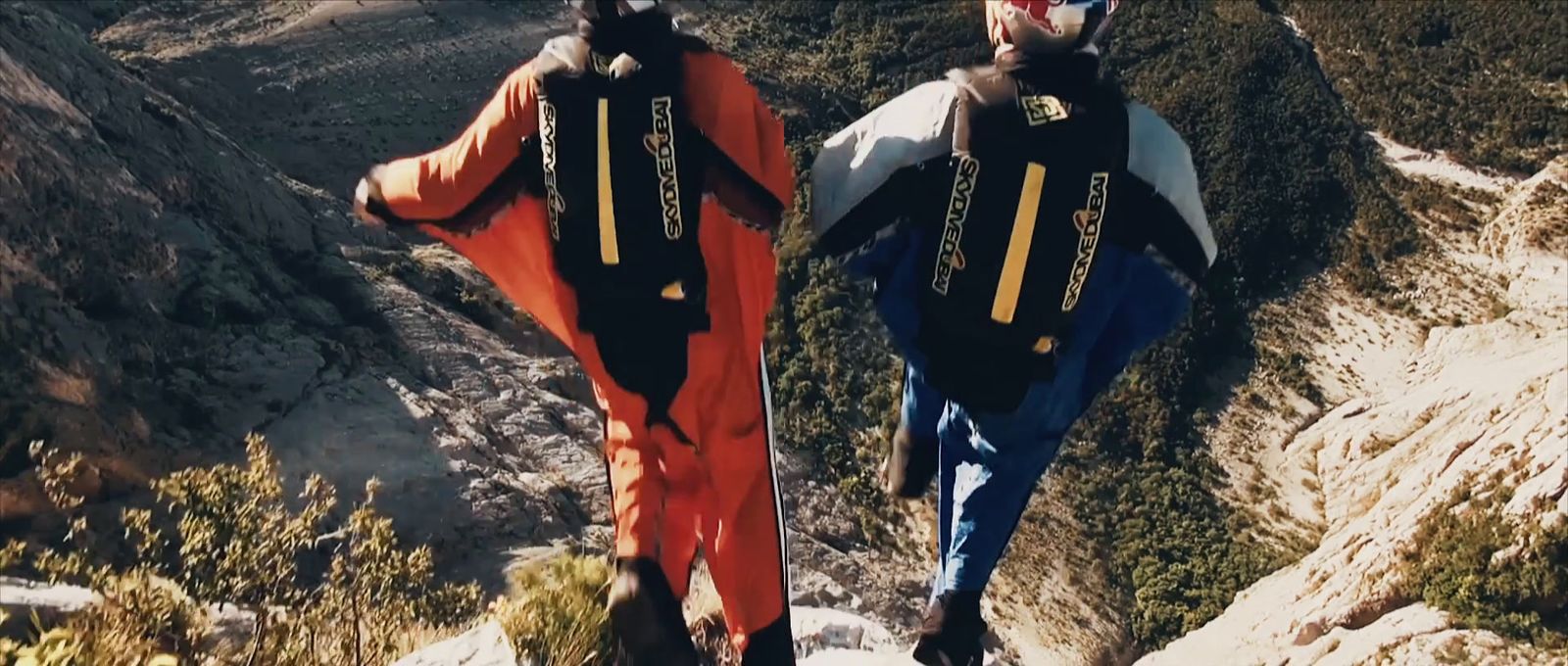 two snowboarders are standing on the edge of a cliff