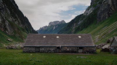 an old stone building in a valley with mountains in the background