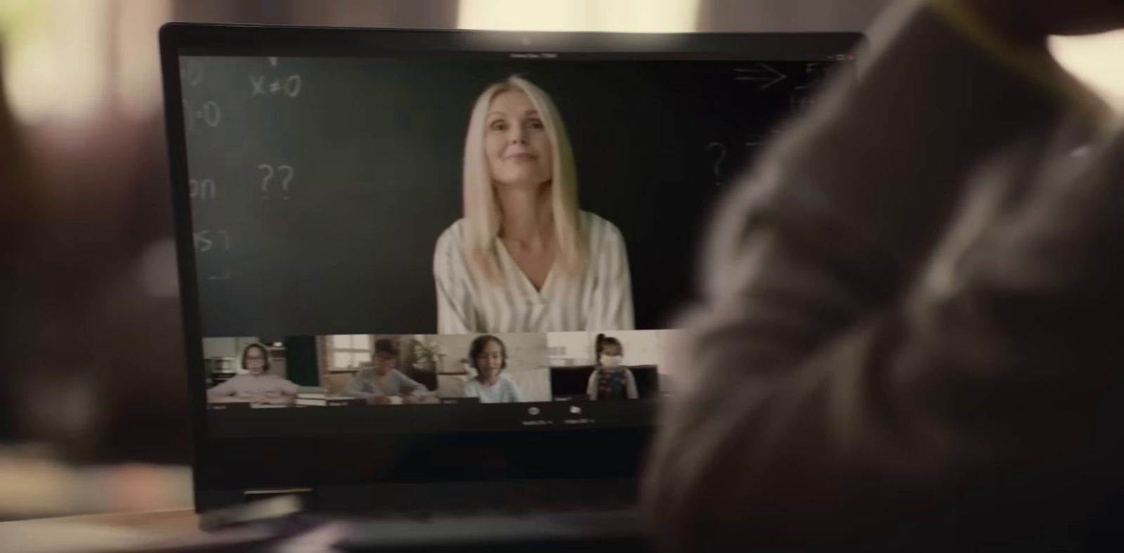 a woman is on a laptop with a group of people on the screen