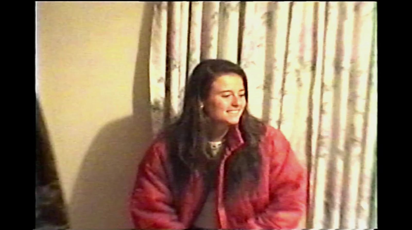 a woman in a red jacket standing in front of a window