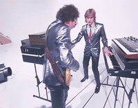 a man in a suit playing a keyboard next to another man in a suit