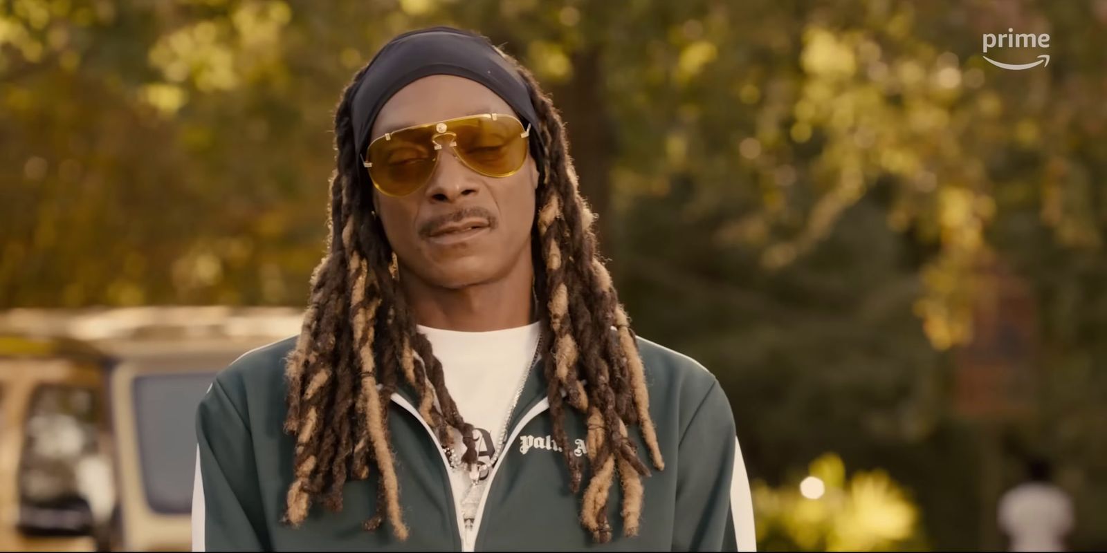 a man with dreadlocks wearing sunglasses and a green jacket