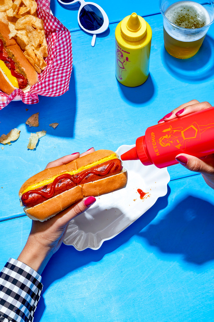 a person holding a hot dog with ketchup and mustard