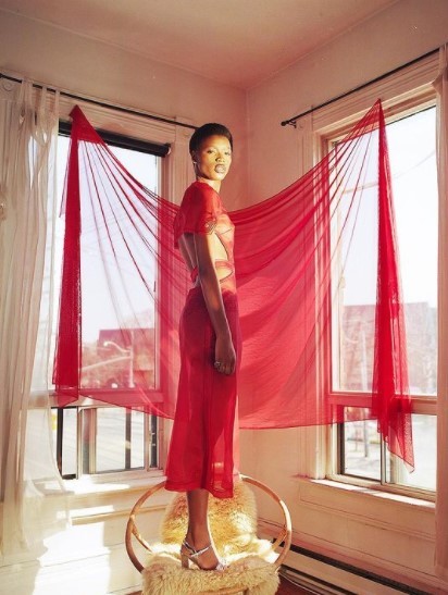 a mannequin dressed in a red dress stands in front of a window