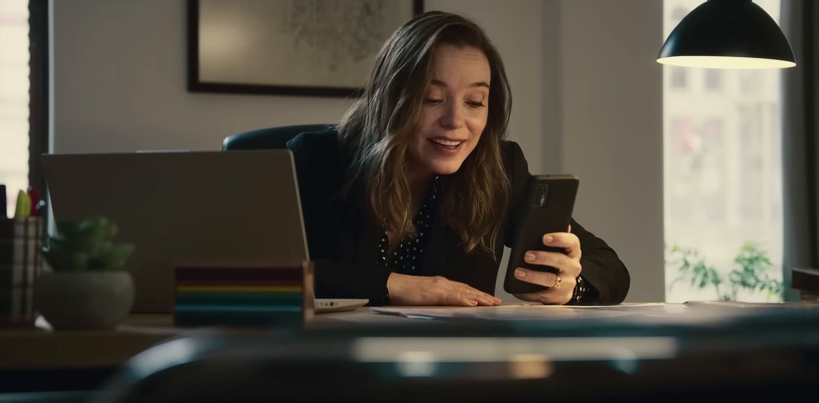 a woman sitting at a desk looking at a cell phone