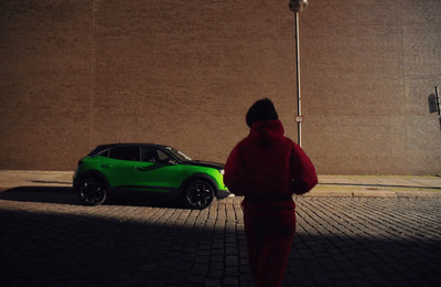 a person walking past a green car on a brick road