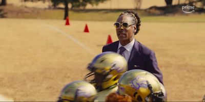 a man in a suit and sunglasses talking to football players