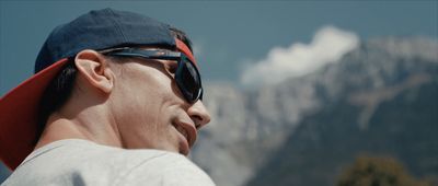 a man wearing sunglasses and a hat with mountains in the background