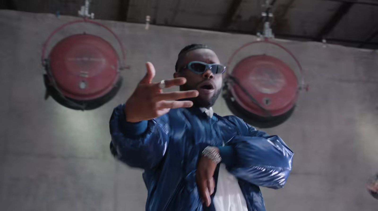 a man in a blue jacket and sunglasses standing in front of a wall