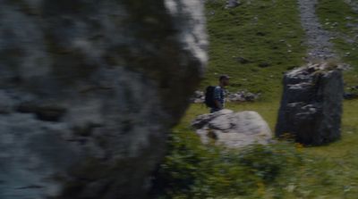 a man standing next to a large rock in a field