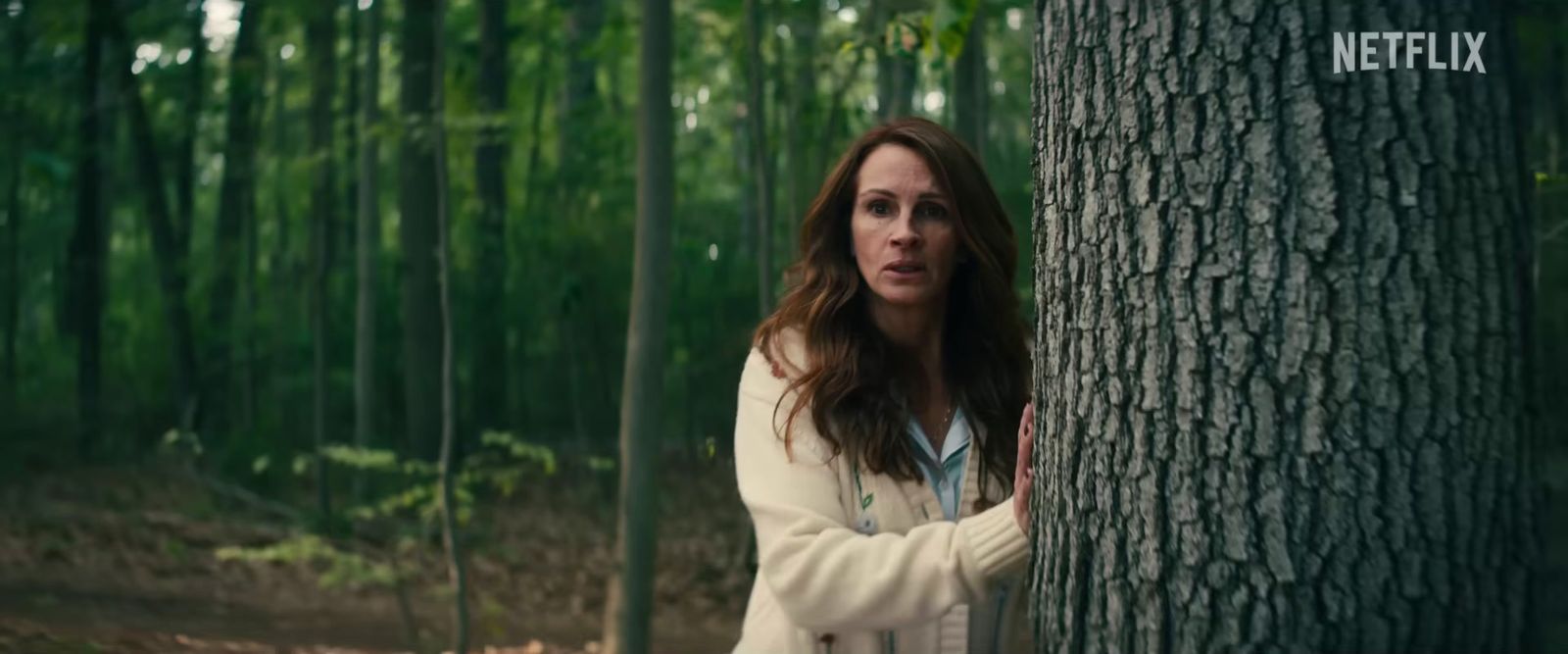 a woman standing next to a tree in a forest